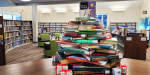 A Christmas-like tree of books with a star-book topper is displayed on top of the bookshelves in the Youth Department at Main.