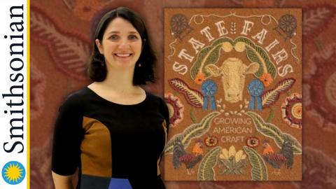Author Mary Savig stands between the Smithsonian logo and a stitched craft that says, "State Fairs. Growing American Craft" and has various animals and farm animals on it.
